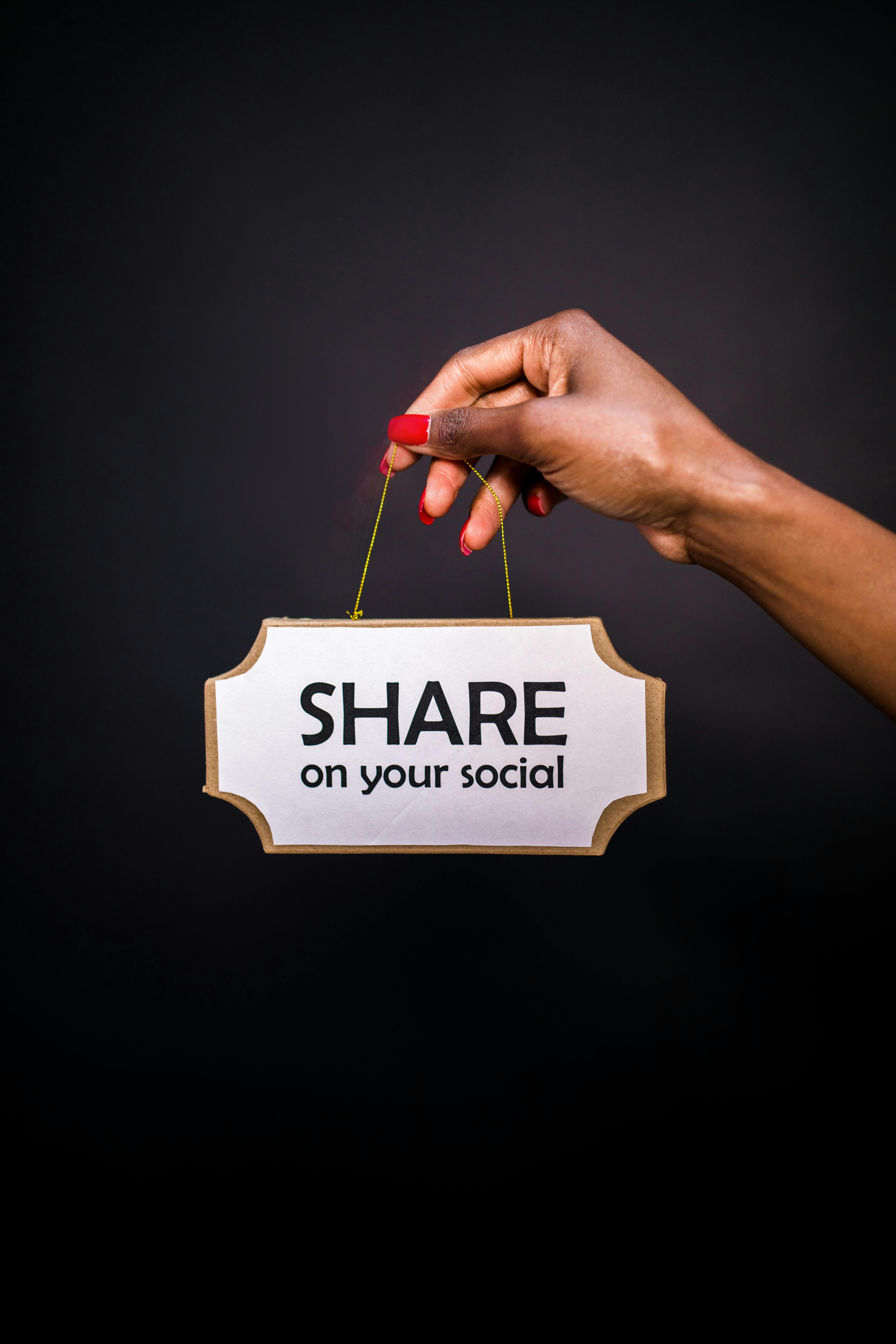 A hand holds a sign reading 'Share on your social' against a dark background.